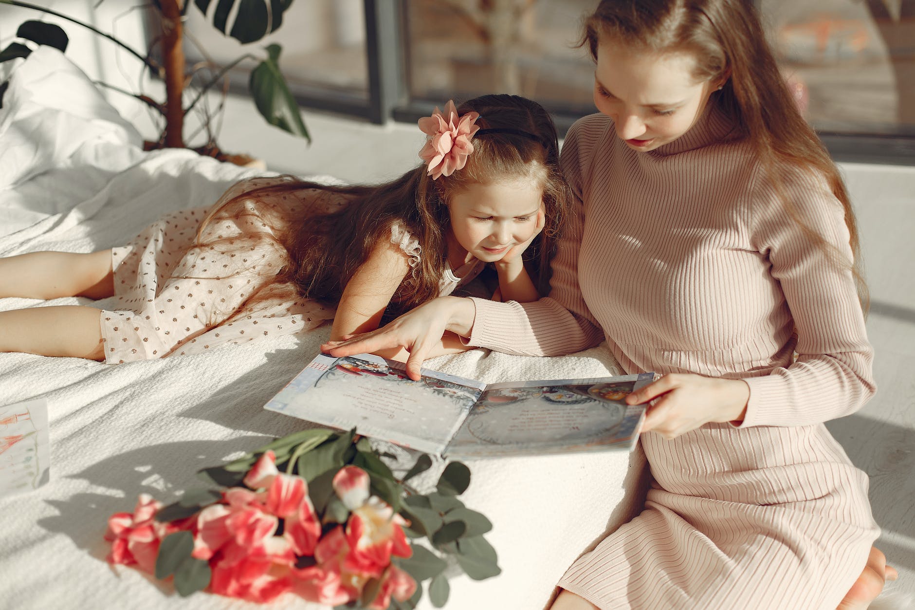 cheerful mother and daughter reading book on bed