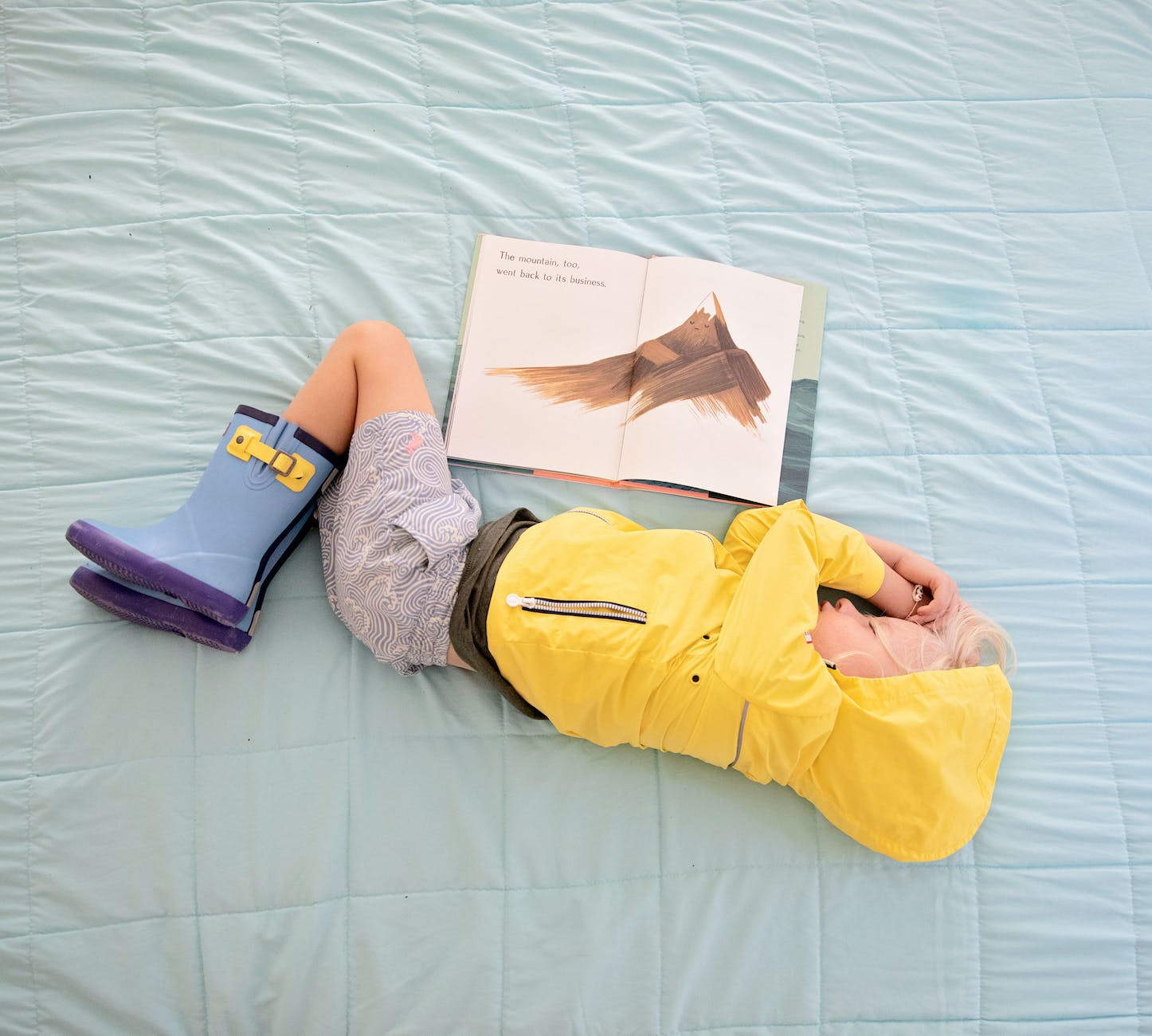 baby in yellow hooded jacket sleeping beside book