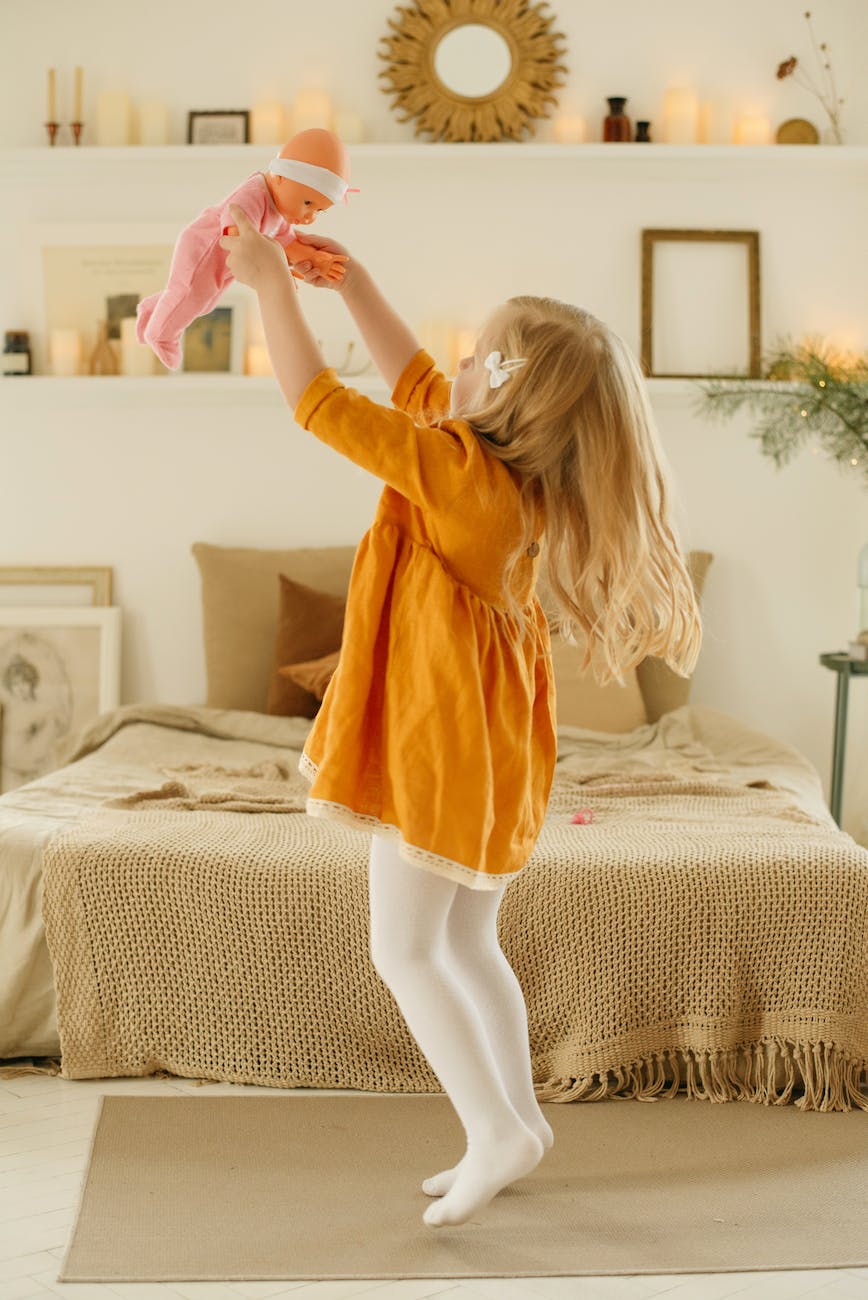 girl in orange dress playing with baby doll