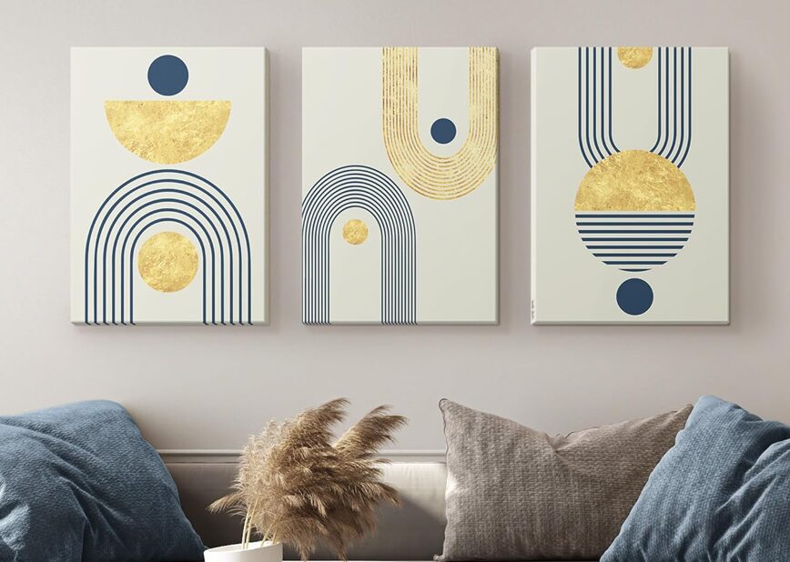 Living room with modern abstract bohemian wall decor featuring geometric shapes and gold accents above a beige sofa, complemented by blue pillows and decorative tables.