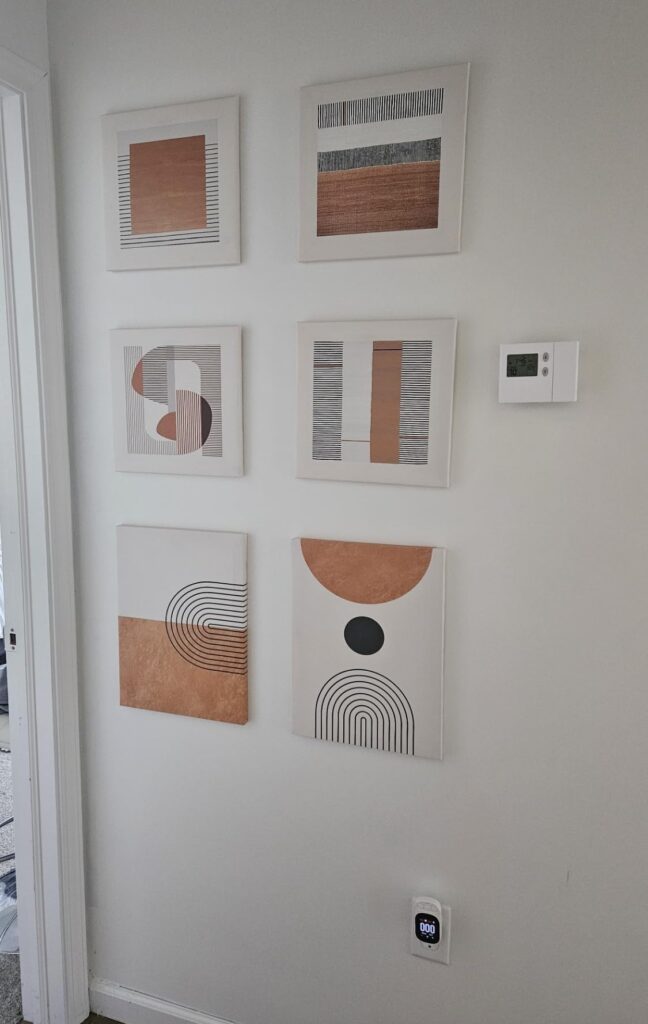 A gallery wall displaying six pieces of bohemian wall decor, each with abstract geometric patterns in shades of orange, black, and white, arranged neatly on a white wall.