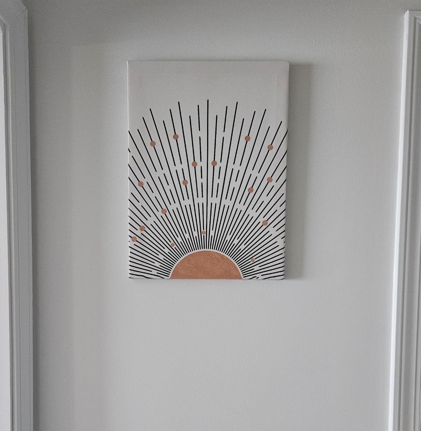 A single piece of bohemian wall decor featuring a sunburst pattern in black and orange, mounted on a light-colored wall.