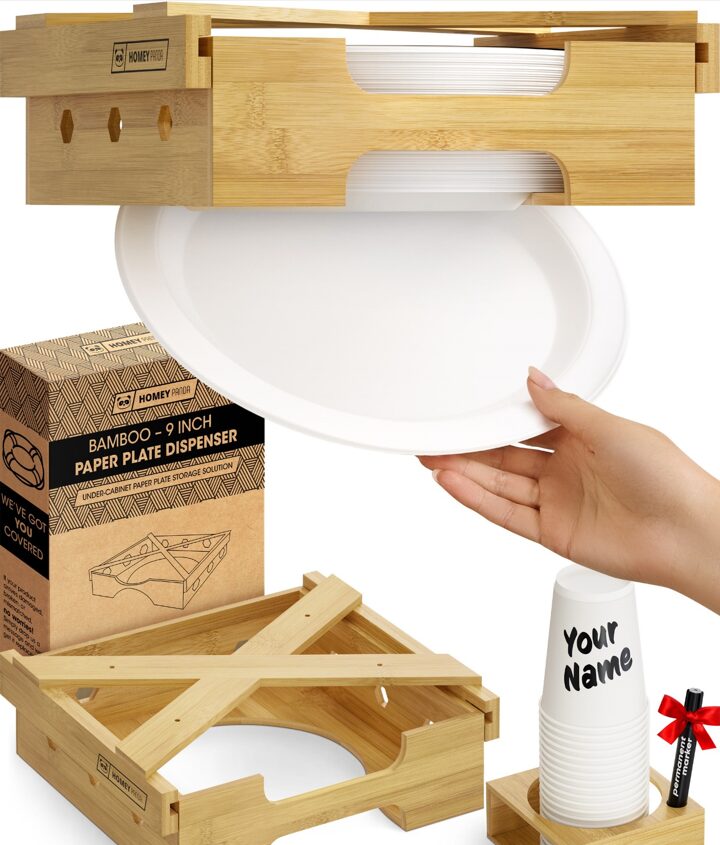 A bamboo paper plate dispenser with a white paper plate being pulled out by a hand. The setup includes the product's packaging, a wooden dispenser and a set of disposable cups with 'Your Name' written on the top cup, along with a red ribboned marker.