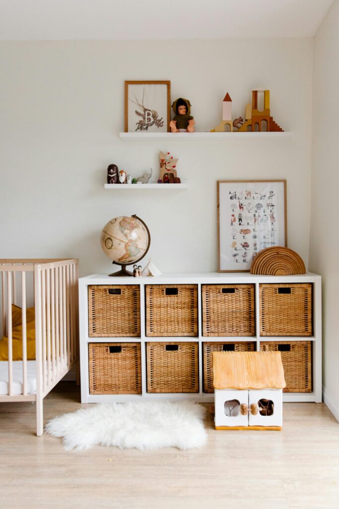 A nursery room with a globe placed on a white shelf unit with wicker baskets. A wall-mounted nursery book shelf above holds toys and decor, while a crib is visible on the side.