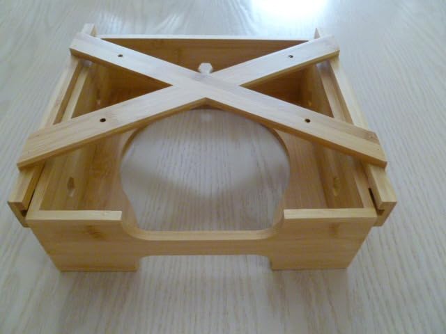 Bamboo paper plate dispenser frame without plates, featuring a cross-shaped support structure and an open circular slot at the base, placed on a light wood surface.