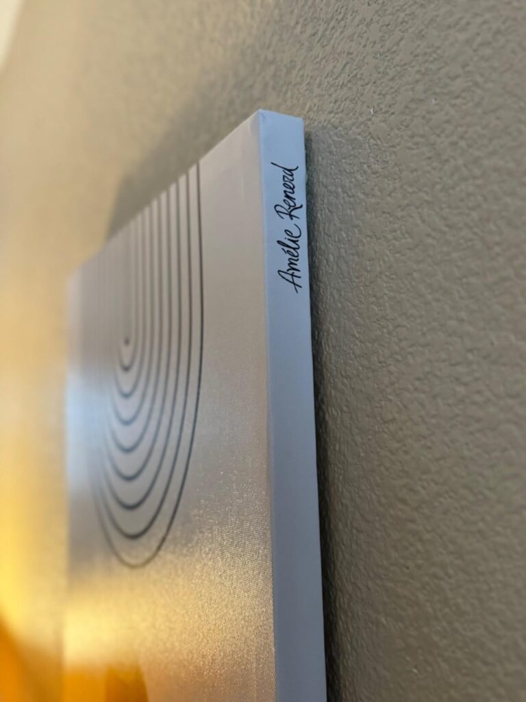 Close-up side view of a boho wall art canvas signed by the artist 'Amelie Reveal,' showcasing the thickness of the canvas against a textured wall