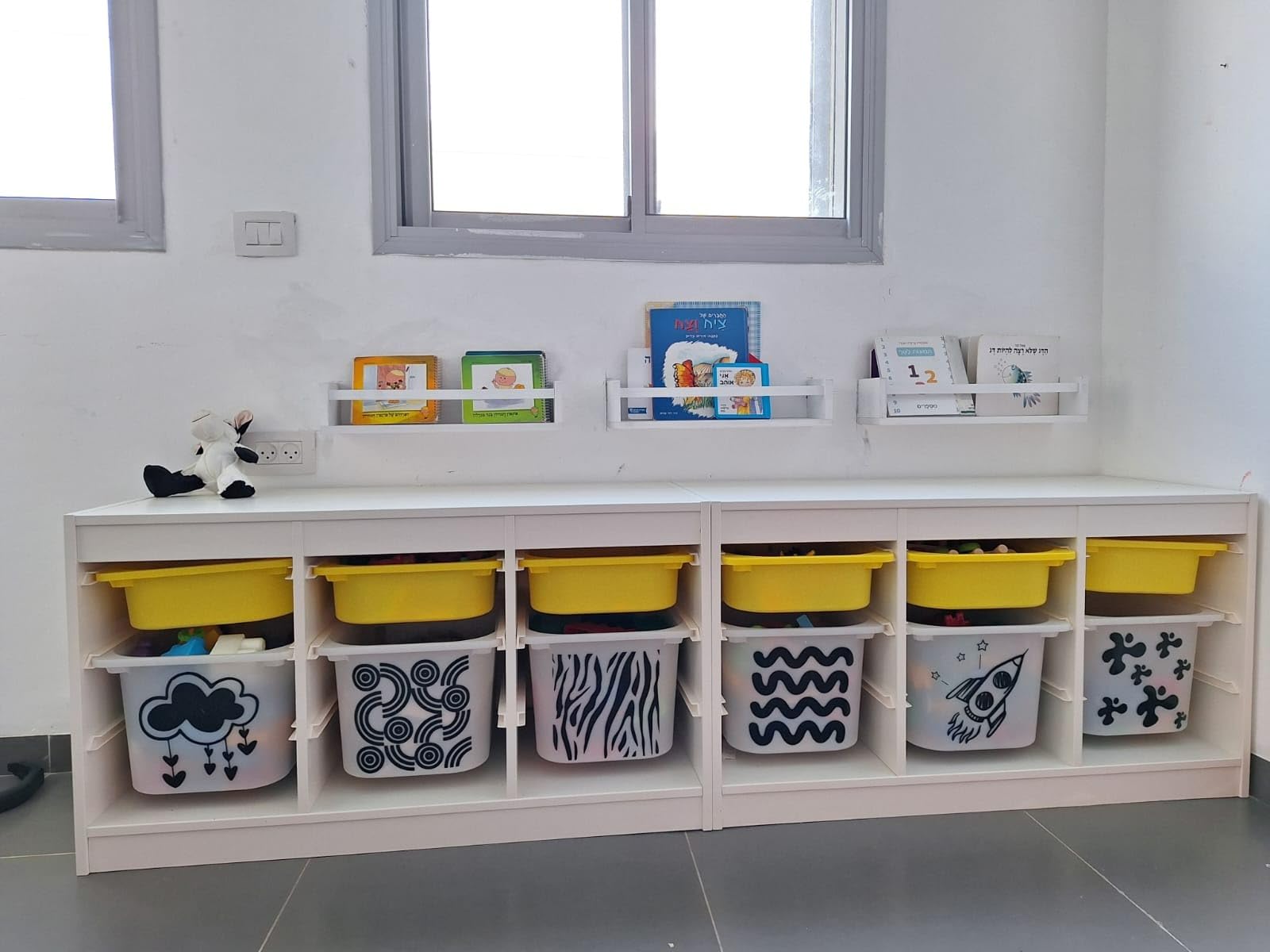 Nursery Shelves for Wall displaying children's books above a white storage unit with yellow bins, creating a neat and organized playroom space