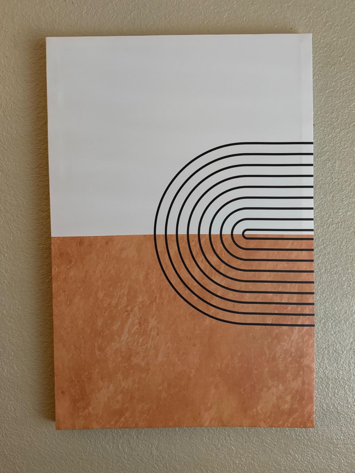 Single piece of boho canvas wall art featuring curved black lines forming a semi-circle on a half-white, half-brown background. A simple yet striking piece of boho canvas wall art for any room.
