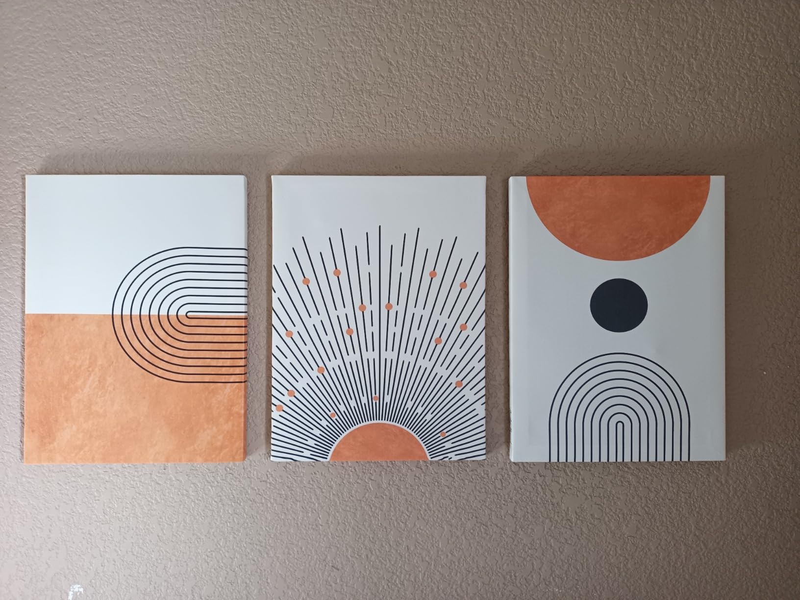 Three-panel boho artwork for wall art featuring minimalist geometric designs in earthy tones. The first panel has curved lines forming a semi-circle, the middle panel showcases sunburst rays with small dots, and the third panel has a circular shape with curved lines below it.