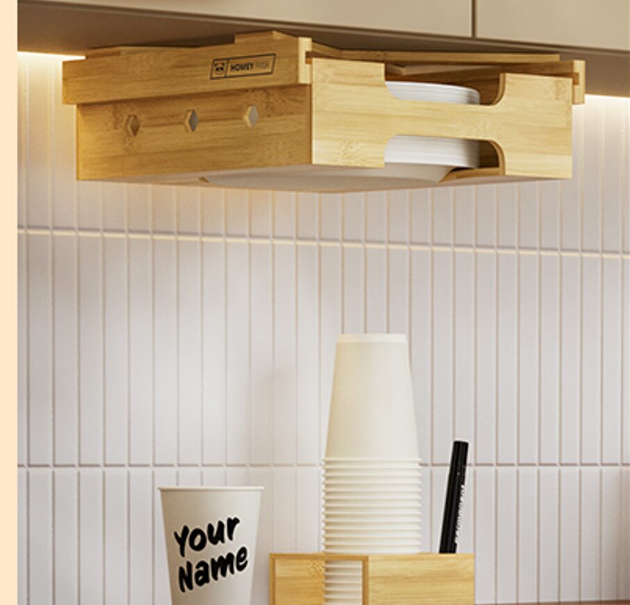Side view of bamboo paper plate holder with hexagonal accents, above stacked cups and a personalized cup on the countertop.