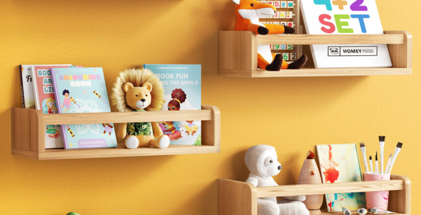 Floating nursery book shelves mounted on a white wall, holding children's books, plush toys, educational blocks, and art supplies. The shelves are in natural wood, with one shelf painted pink, creating a playful and organized display for a child's room.