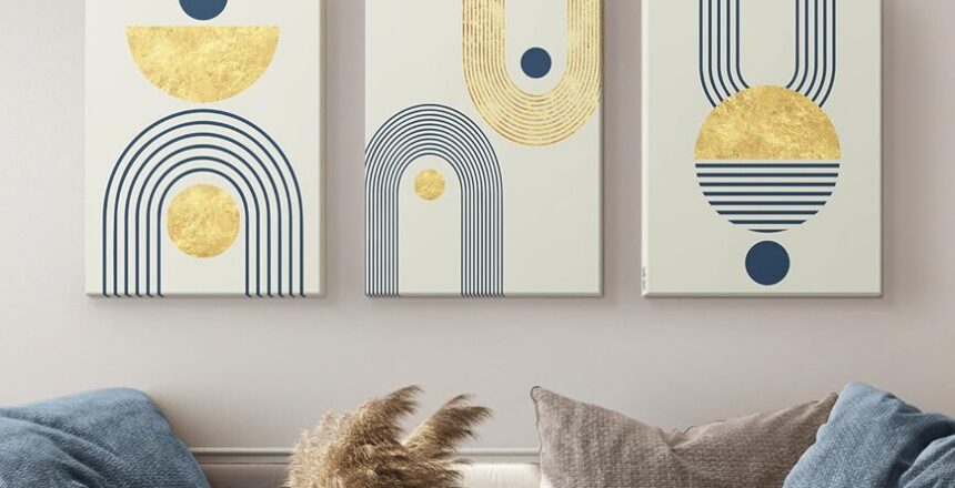 Living room with modern abstract bohemian wall decor featuring geometric shapes and gold accents above a beige sofa, complemented by blue pillows and decorative tables.