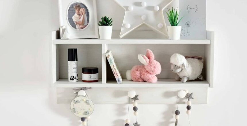 White wall-mounted nursery book shelves with decorative items including a framed photo, star-shaped light, small plants, a pink stuffed bunny, a white stuffed lamb, and string lights with stars hanging below.